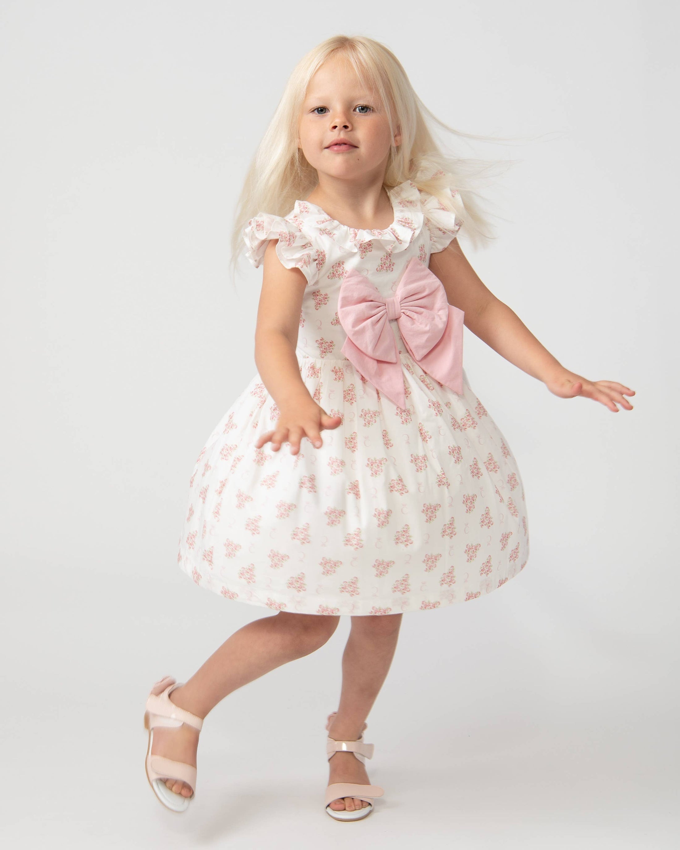 Girl in a white dress with a pink bow spinning happily.